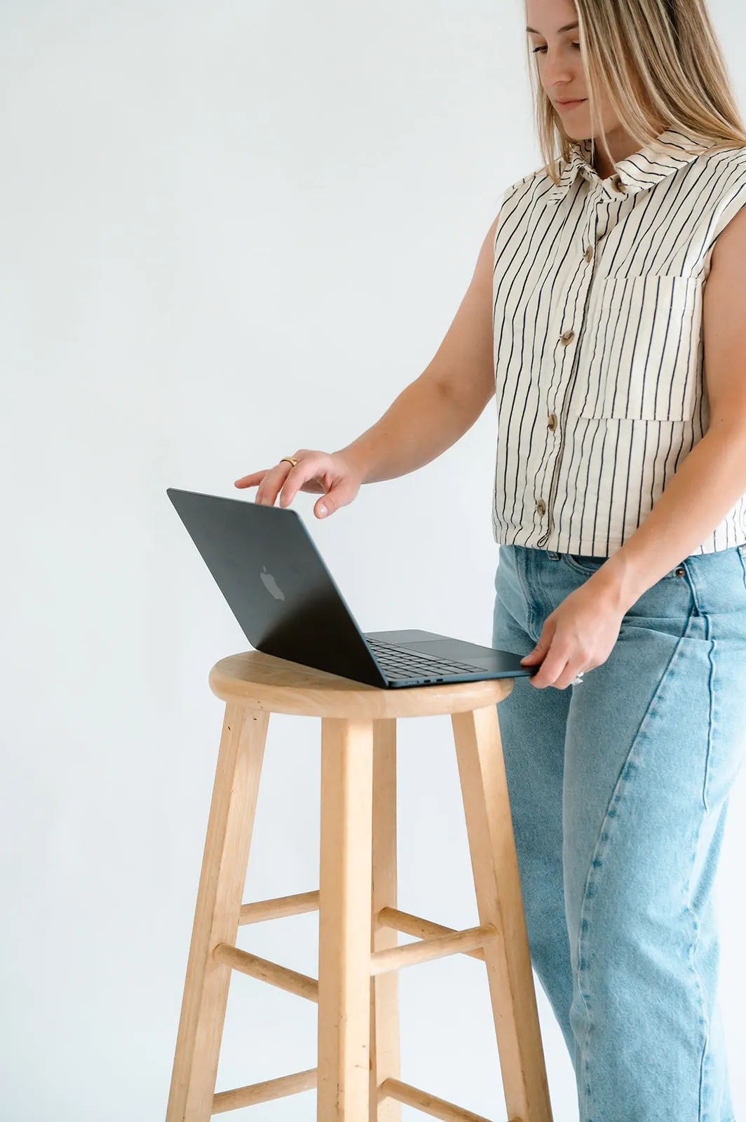 Brooke Kennison opening a laptop on a wooden stool in the studio